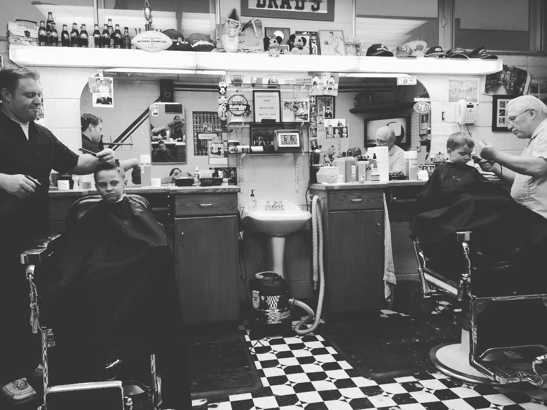 Two barbers cutting hair in the shop's classic barber chairs